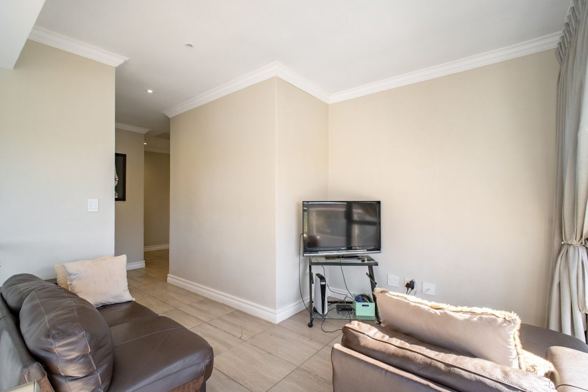 A well-maintained living room featuring neutral tiled flooring, crown molding, and recessed lighting, providing a clean and functional space.