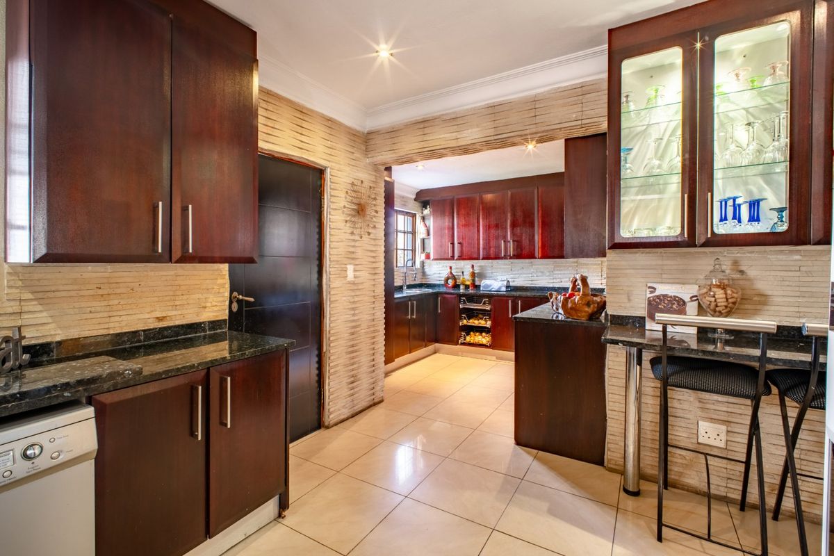 A well-appointed kitchen featuring dark wood cabinetry, granite countertops, and distinctive stacked stone wall finishes with integrated display lighting.