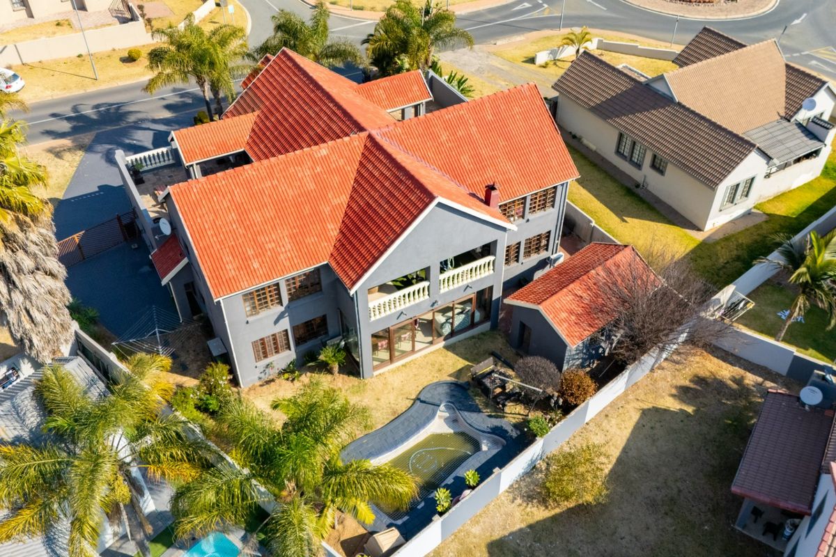 Aerial view of a multi-story residential property featuring a terracotta tile roof, a private swimming pool, and a balcony overlooking the rear garden area.