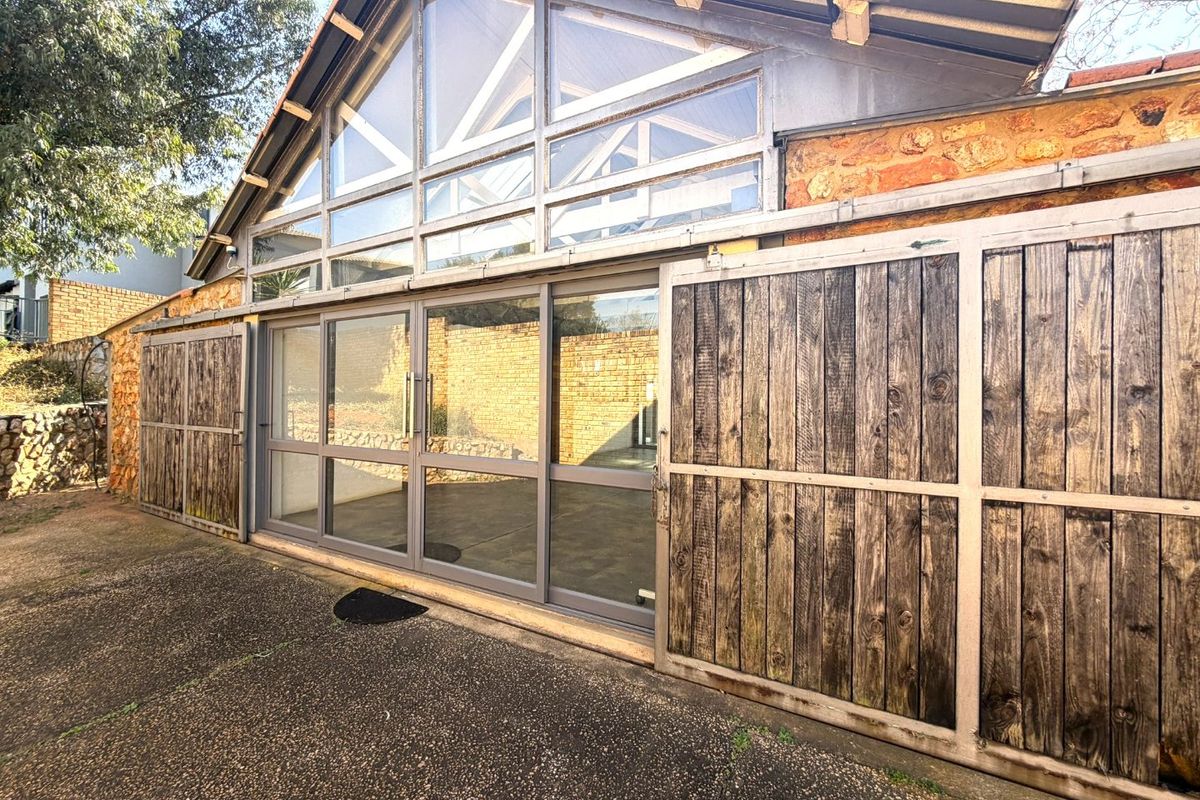 Rear exterior view featuring a large glass facade with sliding doors, timber barn-style shutters, and exposed roof trusses set against a stone wall.