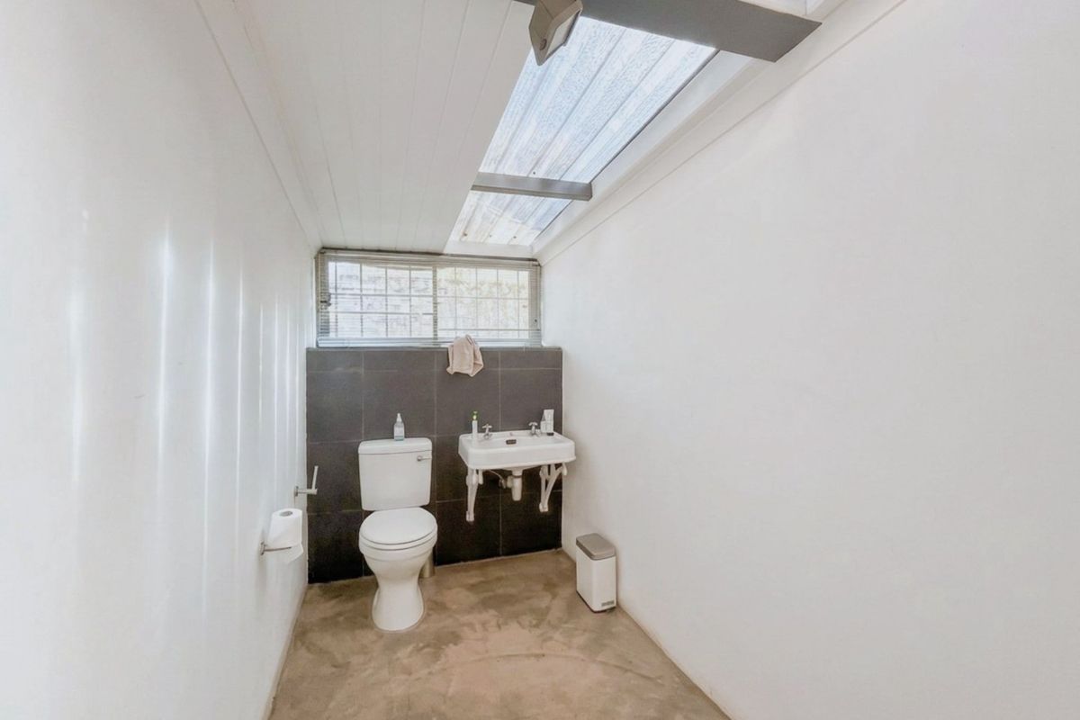 A functional bathroom featuring a toilet, wall-mounted basin, and a skylight, with a minimalist aesthetic and concrete flooring.