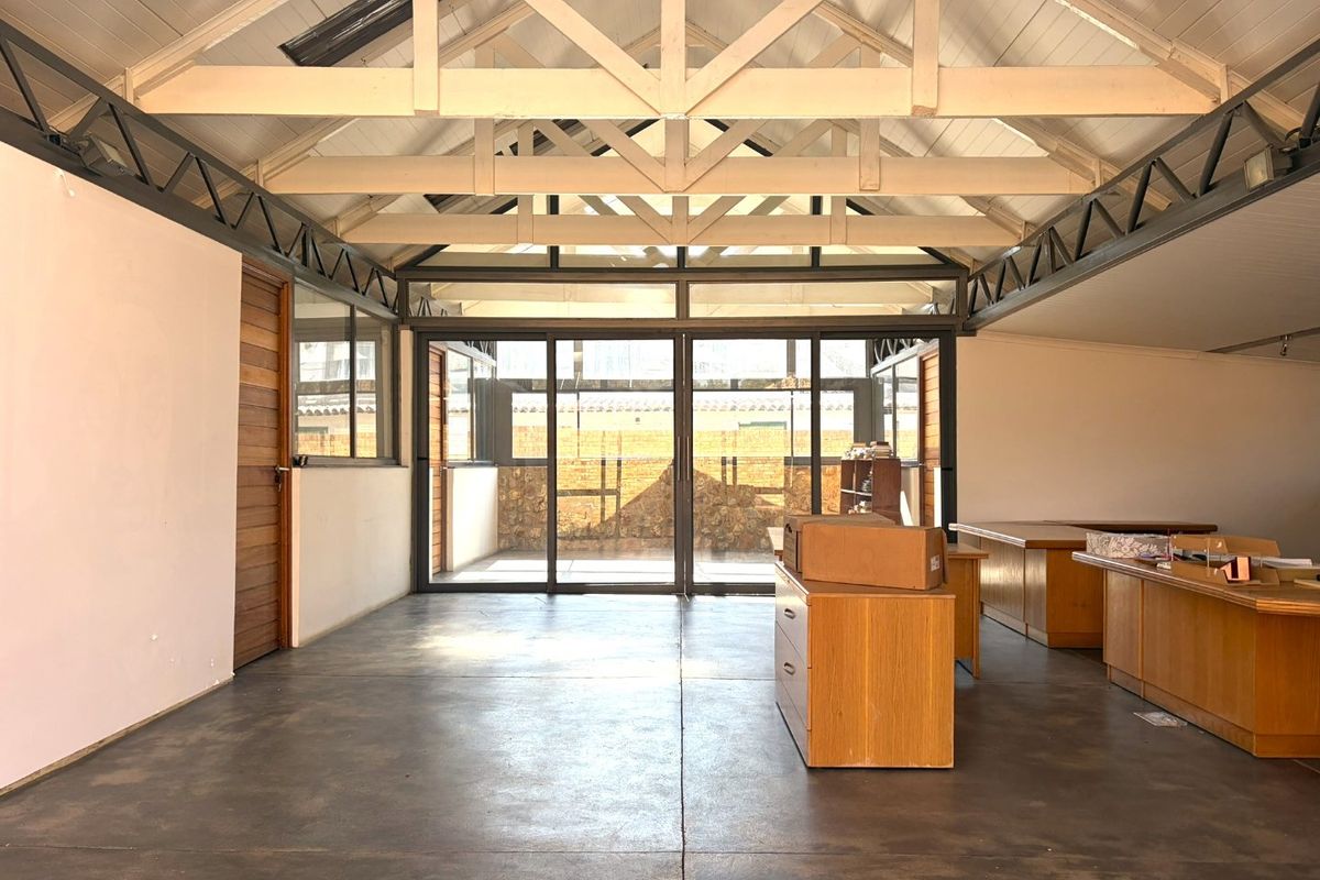 Spacious living area featuring high vaulted ceilings with exposed timber trusses, polished concrete floors, and large sliding glass doors opening to an outdoor space.