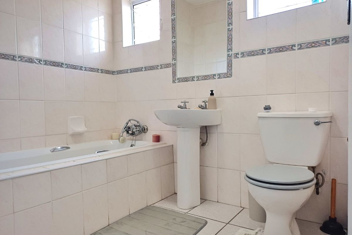 A functional bathroom featuring a pedestal basin, built-in bathtub, and toilet with neutral ceramic wall and floor tiling.