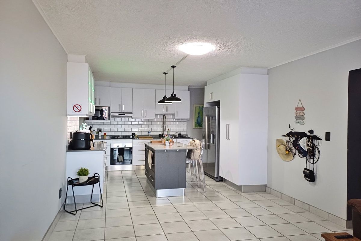 A well-maintained kitchen featuring white cabinetry, a central island, subway tile backsplash, and modern built-in appliances with tiled flooring throughout.