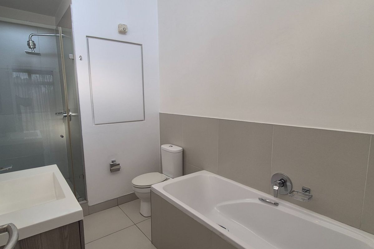A modern, clean bathroom featuring a separate shower enclosure, a bathtub, a vanity basin, and neutral wall tiling.