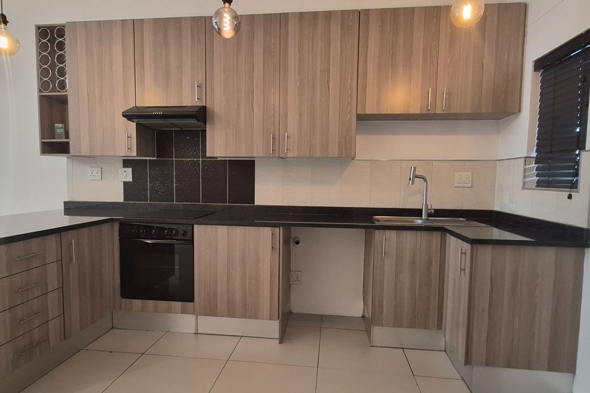 Modern kitchen featuring wood-look laminate cabinetry, black stone countertops, built-in oven, extractor fan, and tiled flooring in a clean, functional layout.
