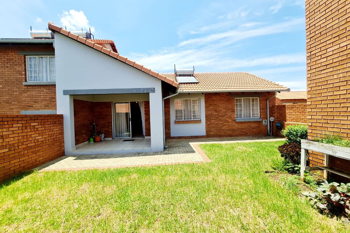 Rear view of the property featuring a brick facade, a covered patio area, a paved walkway, and a private lawn.