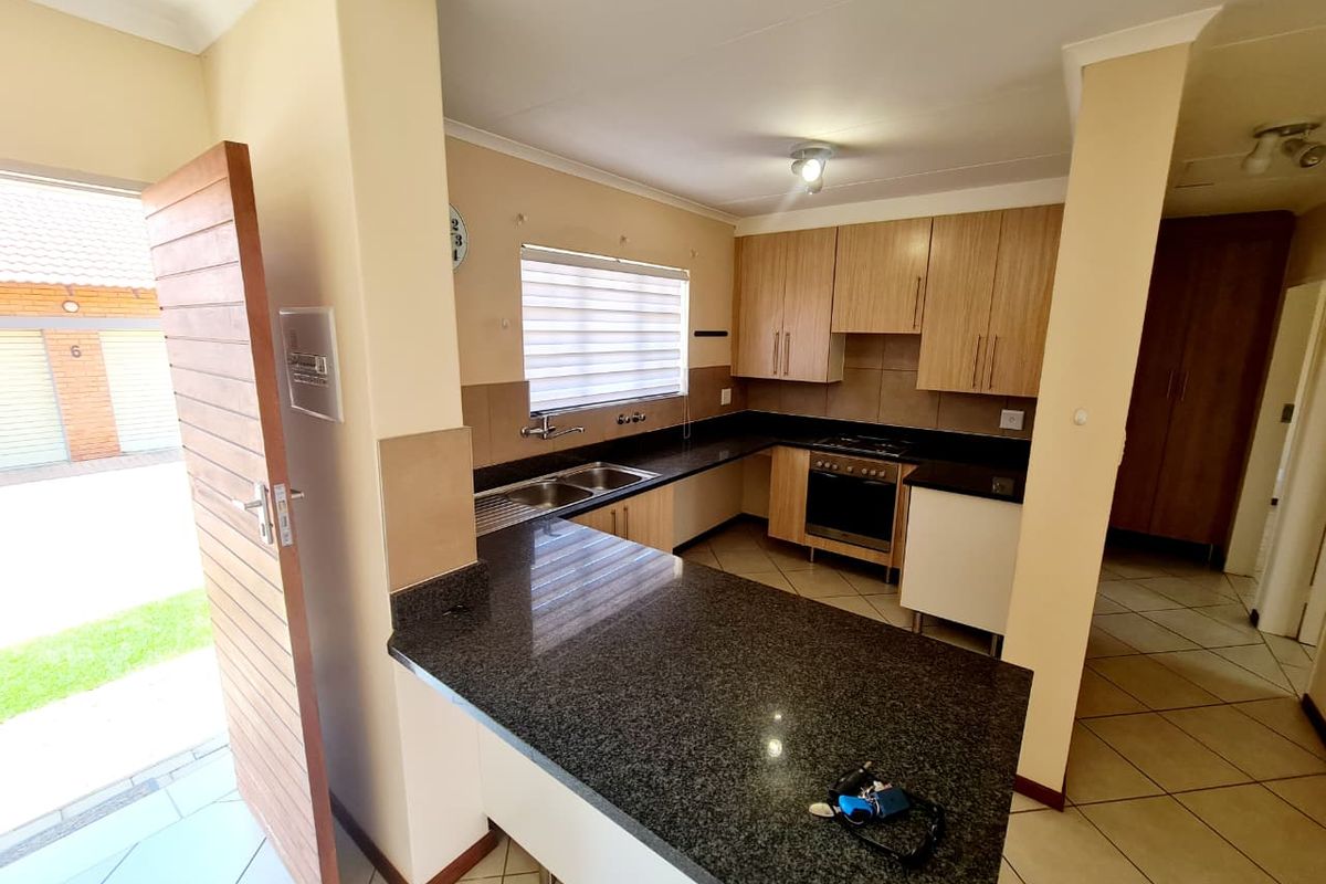 A functional kitchen featuring granite countertops, wooden cabinetry, built-in oven, gas hob, and tiled flooring, with direct access to the exterior.
