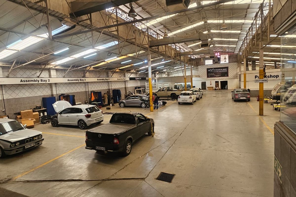 Spacious industrial workshop featuring high steel truss ceilings, concrete flooring, and designated assembly bays, suitable for automotive repair or manufacturing operations.