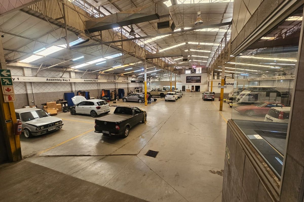 Large industrial workshop space featuring high ceilings with exposed steel trusses, concrete flooring, and integrated ventilation systems, suitable for automotive assembly or storage.