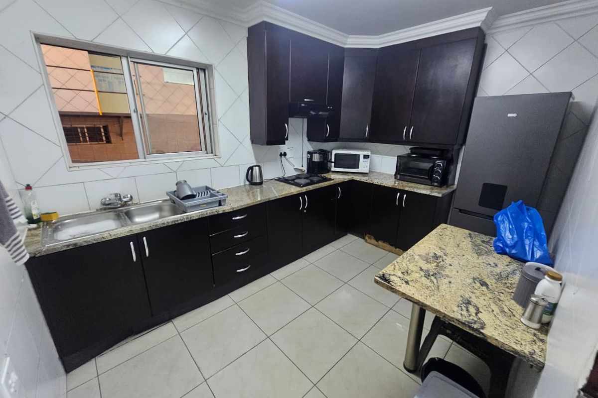 Functional kitchen featuring dark wood cabinetry, granite countertops, double basin sink, and tiled finishes, offering a practical workspace for industrial or commercial use.