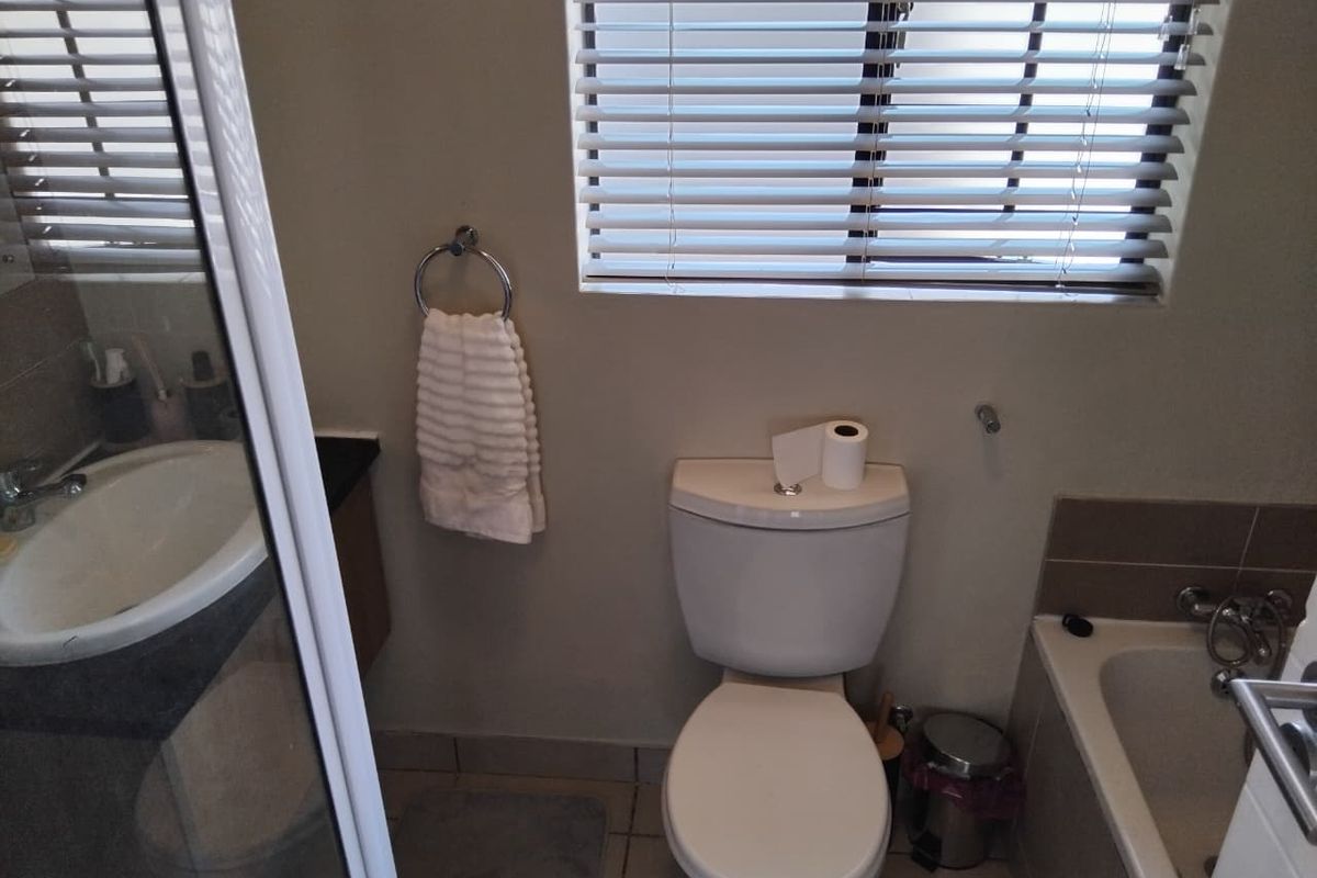 A functional bathroom featuring a toilet, bathtub, separate shower enclosure, and a vanity basin with neutral wall finishes and window blinds.