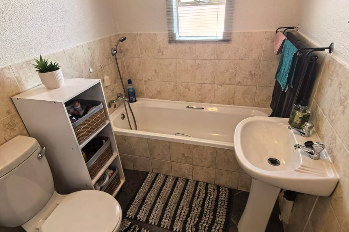 A functional bathroom featuring a bathtub with shower mixer, pedestal basin, and toilet, finished with neutral wall and floor tiling.