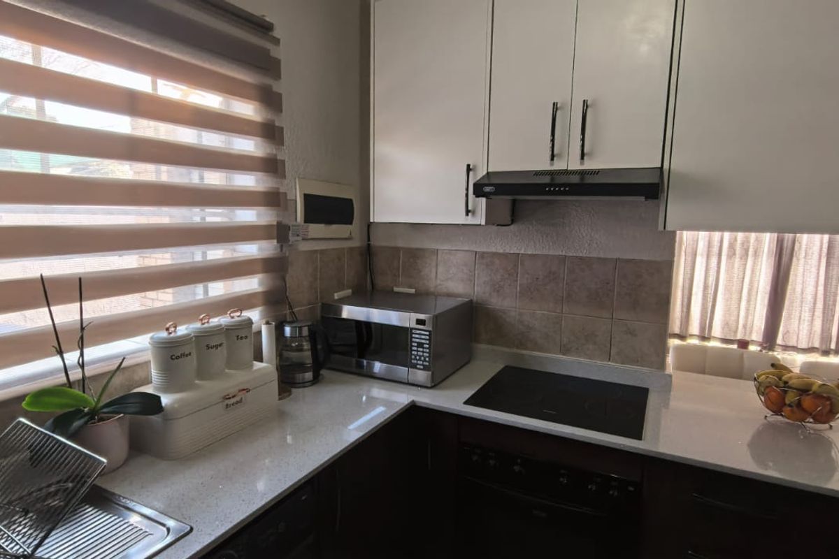 A functional kitchen featuring modern white upper cabinetry, dark lower cabinets, stone countertops, an electric hob, and a tiled backsplash.