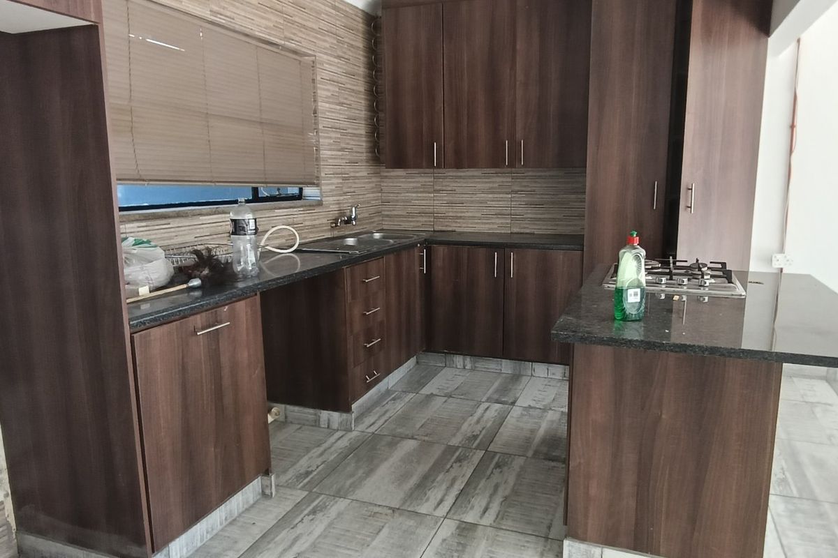 A functional kitchen featuring dark wood cabinetry, granite countertops, a built-in gas hob, and tiled flooring, offering a clean and practical workspace.