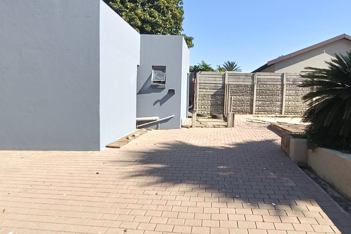 A rear exterior view featuring a paved patio area, precast concrete boundary wall, and a retaining wall structure.