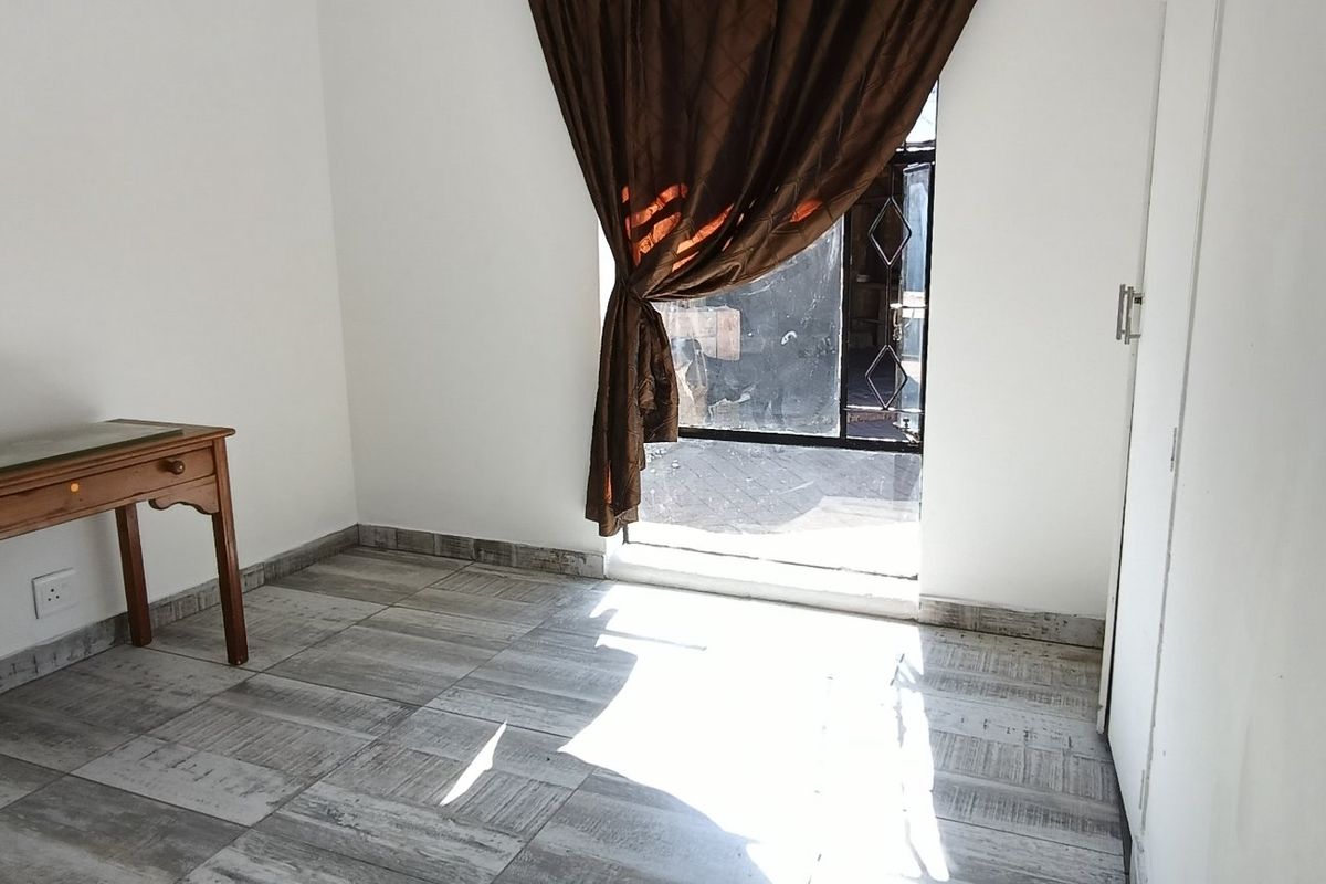 A bright, empty bedroom featuring tiled flooring, a built-in cupboard, and a security gate leading to the exterior.