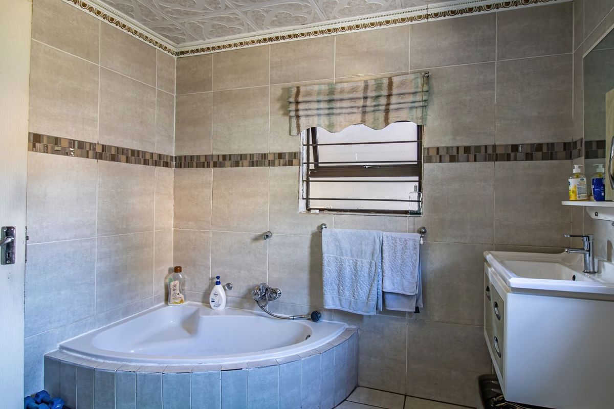 A functional bathroom featuring a corner bathtub, vanity basin, and neutral wall tiling with decorative accents and a window with security bars.