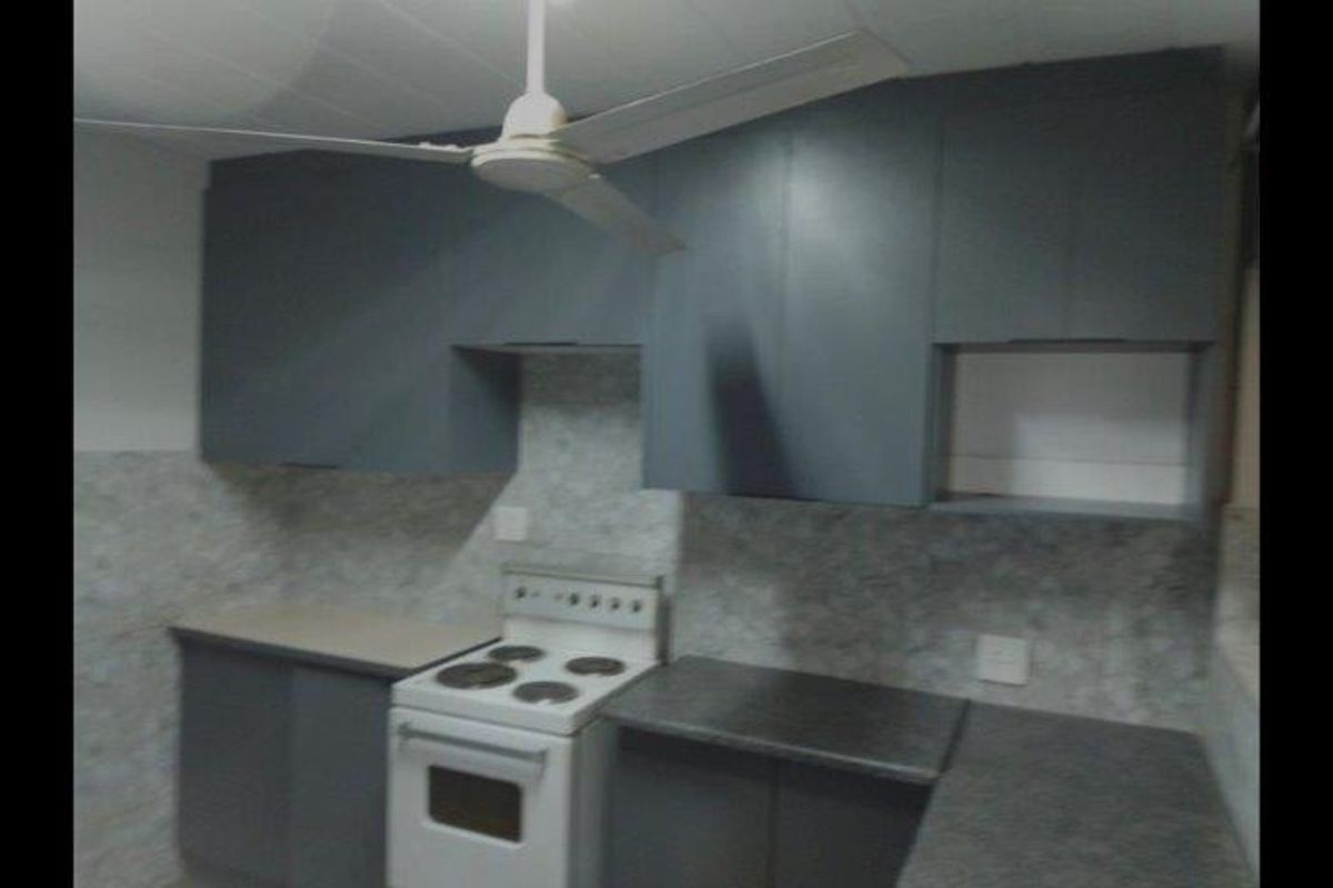 A functional kitchen featuring grey built-in cabinetry, laminate countertops, a tiled backsplash, and a freestanding stove.