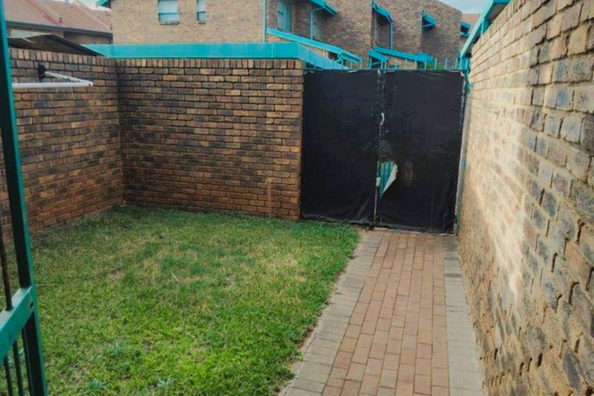 A private rear courtyard featuring a brick boundary wall, paved walkway, and a small lawn area with a gated entrance.