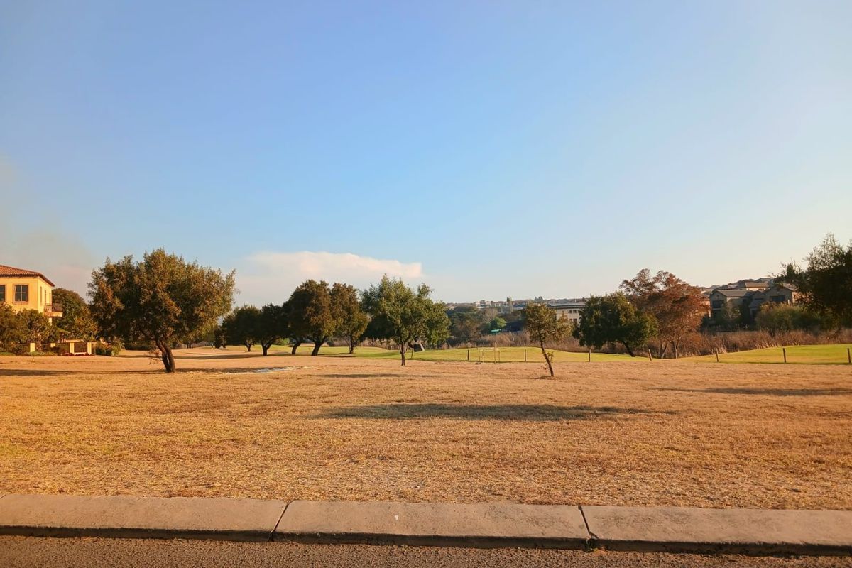 A view of a vacant residential plot featuring open grassland and mature trees, situated in a quiet neighborhood setting.