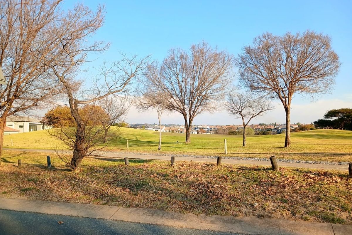 A scenic view of a well-maintained residential green space featuring mature trees, manicured lawns, and a paved walking path.