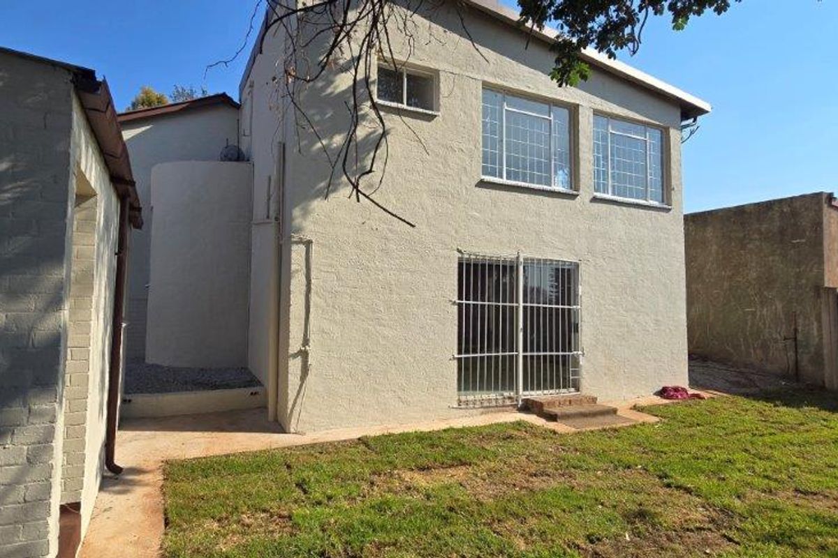 Rear view of the property featuring plastered exterior walls, security bars on windows and doors, and a small garden area.