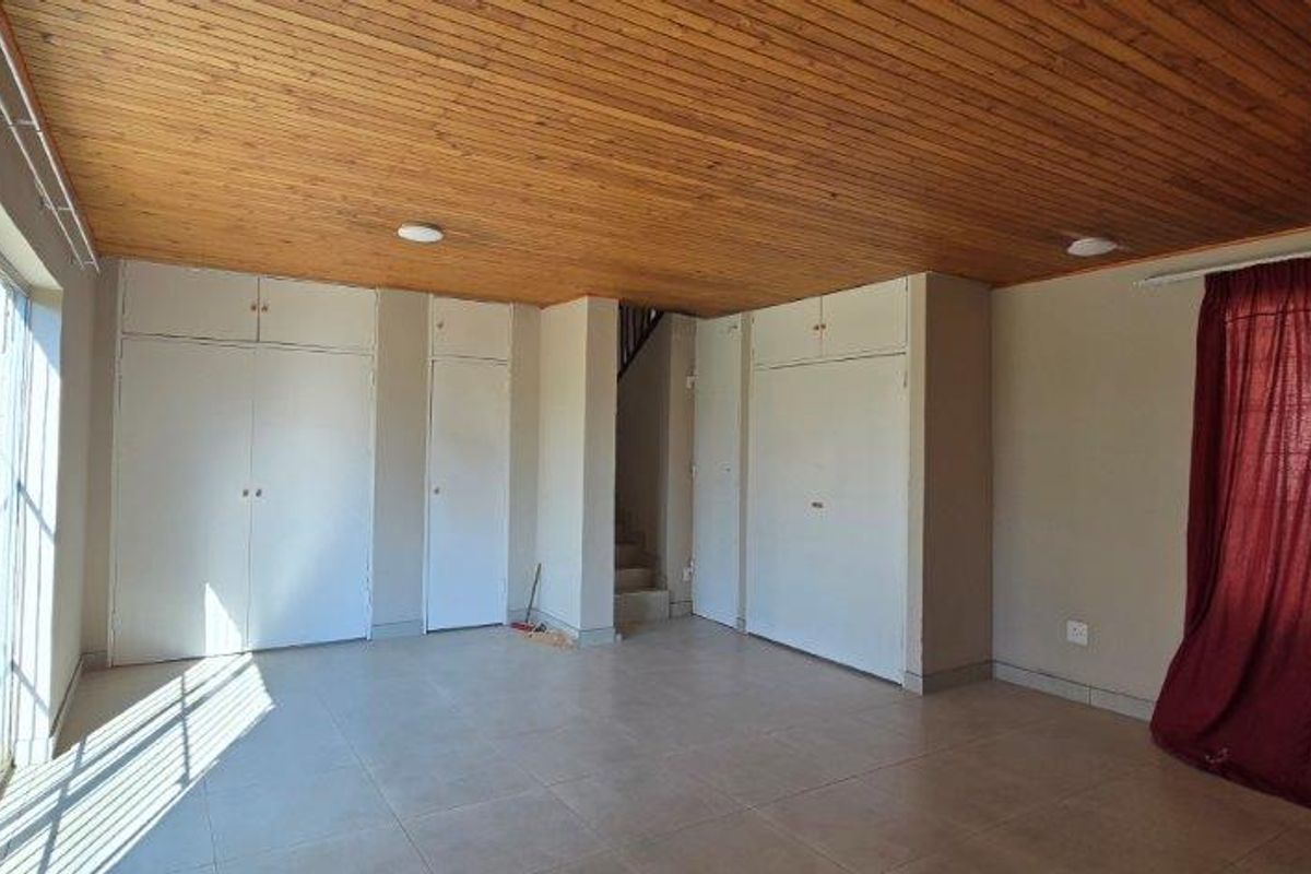 Spacious living area featuring a timber-clad ceiling, tiled flooring, and extensive built-in storage cupboards, with direct access to an outdoor area via sliding doors.