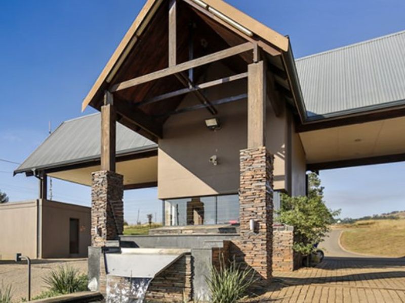 A well-maintained entrance gatehouse featuring stone cladding, timber structural elements, and a decorative water feature, set within a residential estate.