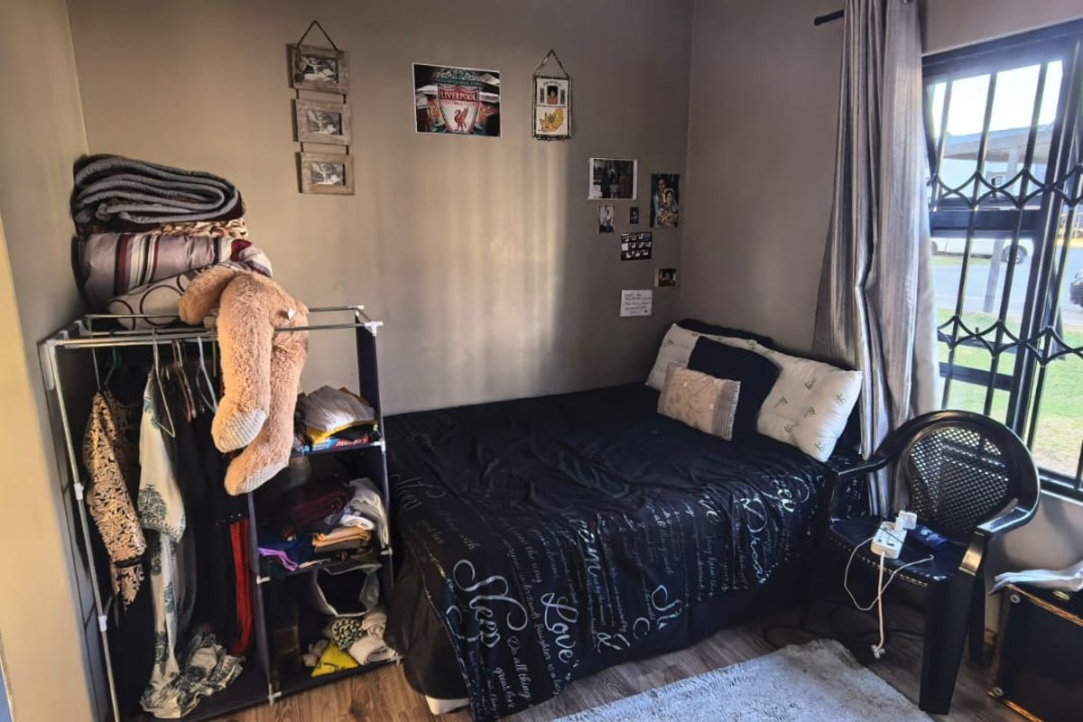 A compact bedroom featuring laminate flooring and a window fitted with security bars, providing natural light and street-facing views.