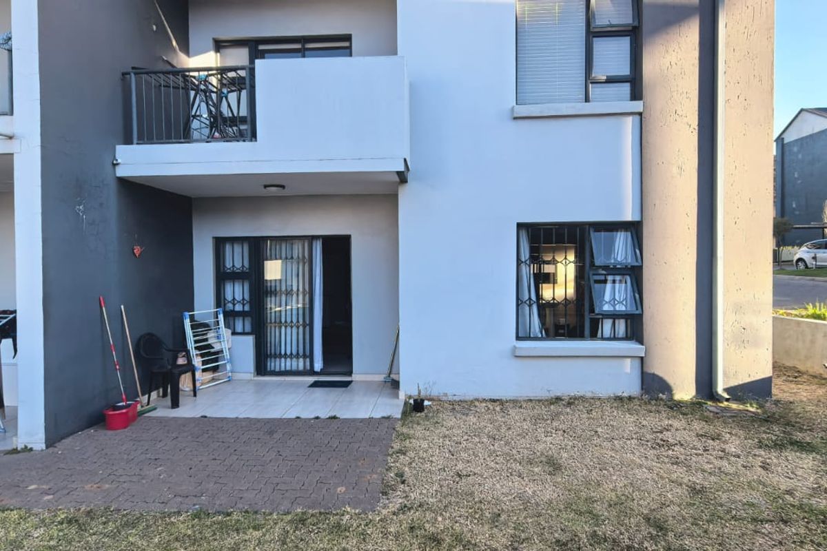 Rear view of the apartment featuring a paved patio area, a small balcony above, and secure metal window and door fittings.