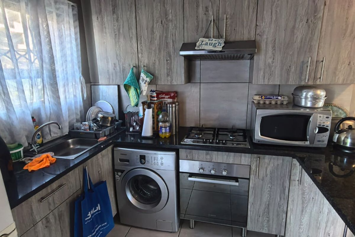 Compact kitchen featuring wood-look cabinetry, granite countertops, a gas hob, built-in oven, extractor fan, and an integrated washing machine.