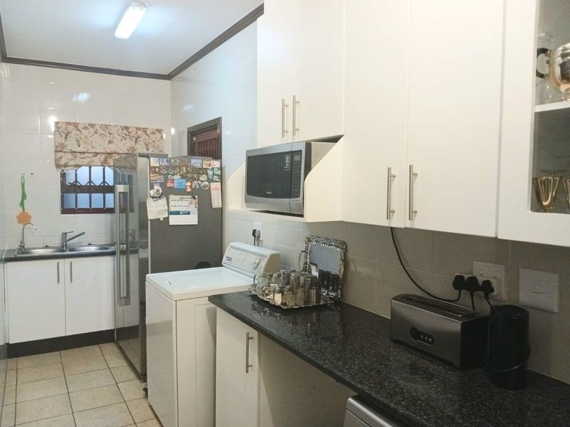 A functional kitchen featuring white cabinetry, dark granite countertops, tiled splashbacks, and integrated appliance spaces.