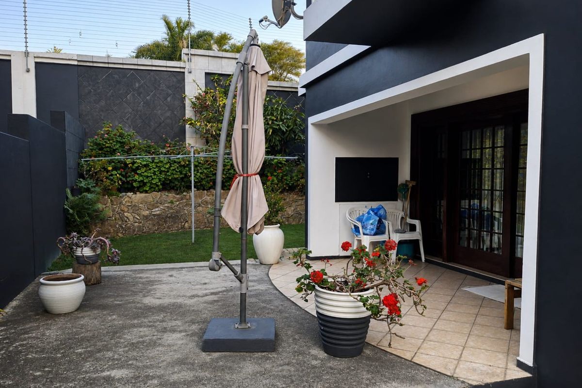 Rear exterior view featuring a tiled patio area, concrete paving, stone retaining wall, and secure perimeter electric fencing.