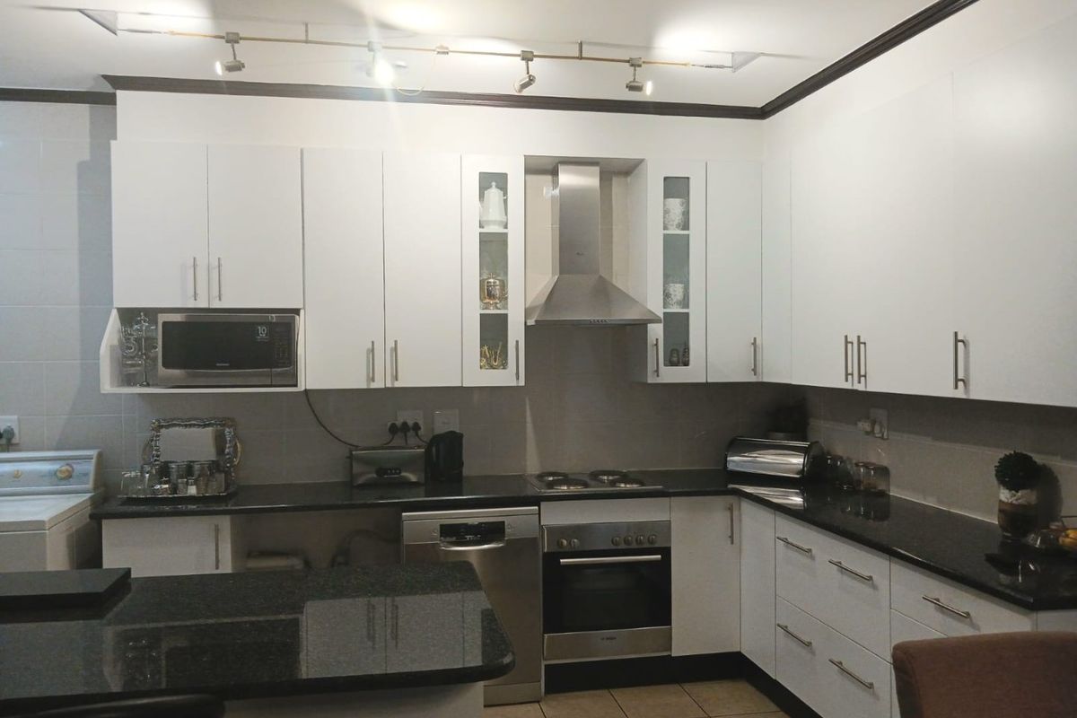 Modern kitchen featuring white cabinetry, dark granite countertops, stainless steel appliances, and functional track lighting, providing a clean and efficient workspace.