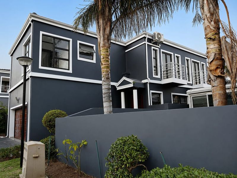 A modern double-story residential facade featuring dark grey exterior paint, white trim, balconies, and an integrated garage.