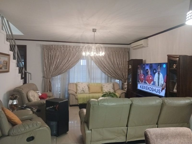 A comfortable living room featuring tiled flooring, a staircase, and a wall-mounted air conditioning unit.