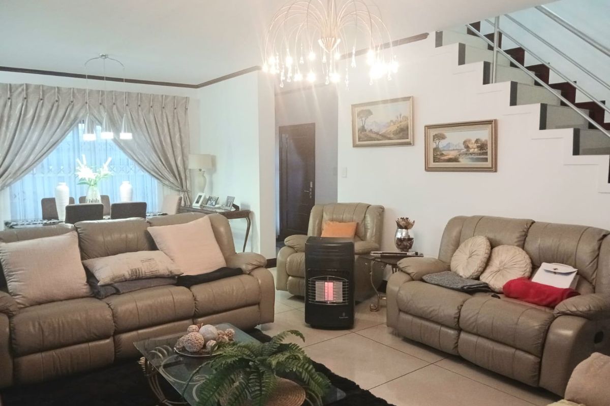 A spacious living room featuring large floor tiles, a modern staircase with metal balustrades, and an elegant chandelier, creating a bright and welcoming atmosphere.