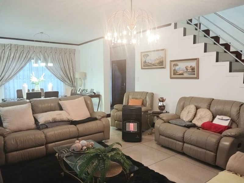 A spacious living room featuring large floor tiles, a modern staircase with metal balustrades, and an elegant chandelier, creating a bright and welcoming atmosphere.