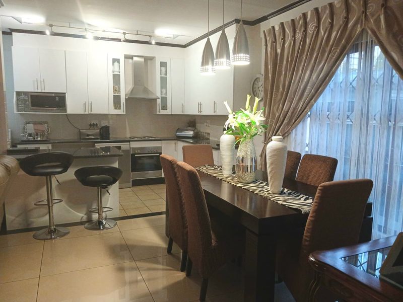 Open-plan kitchen and dining area featuring modern white cabinetry, granite countertops, stainless steel appliances, and tiled flooring with integrated lighting.