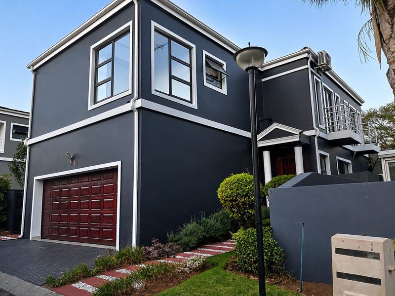 Modern two-story house featuring a dark exterior finish, double garage, balcony, and well-maintained front garden with paved driveway.