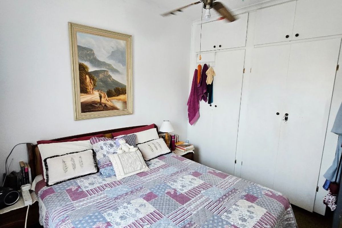 A functional bedroom featuring built-in cupboards and a ceiling fan, offering a practical layout with neutral wall finishes.