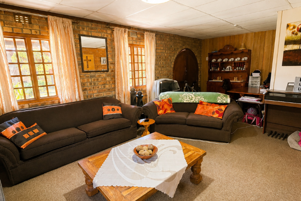 A living room featuring exposed brick walls, wood paneling, and timber-framed windows, finished with a suspended ceiling and carpeted flooring.