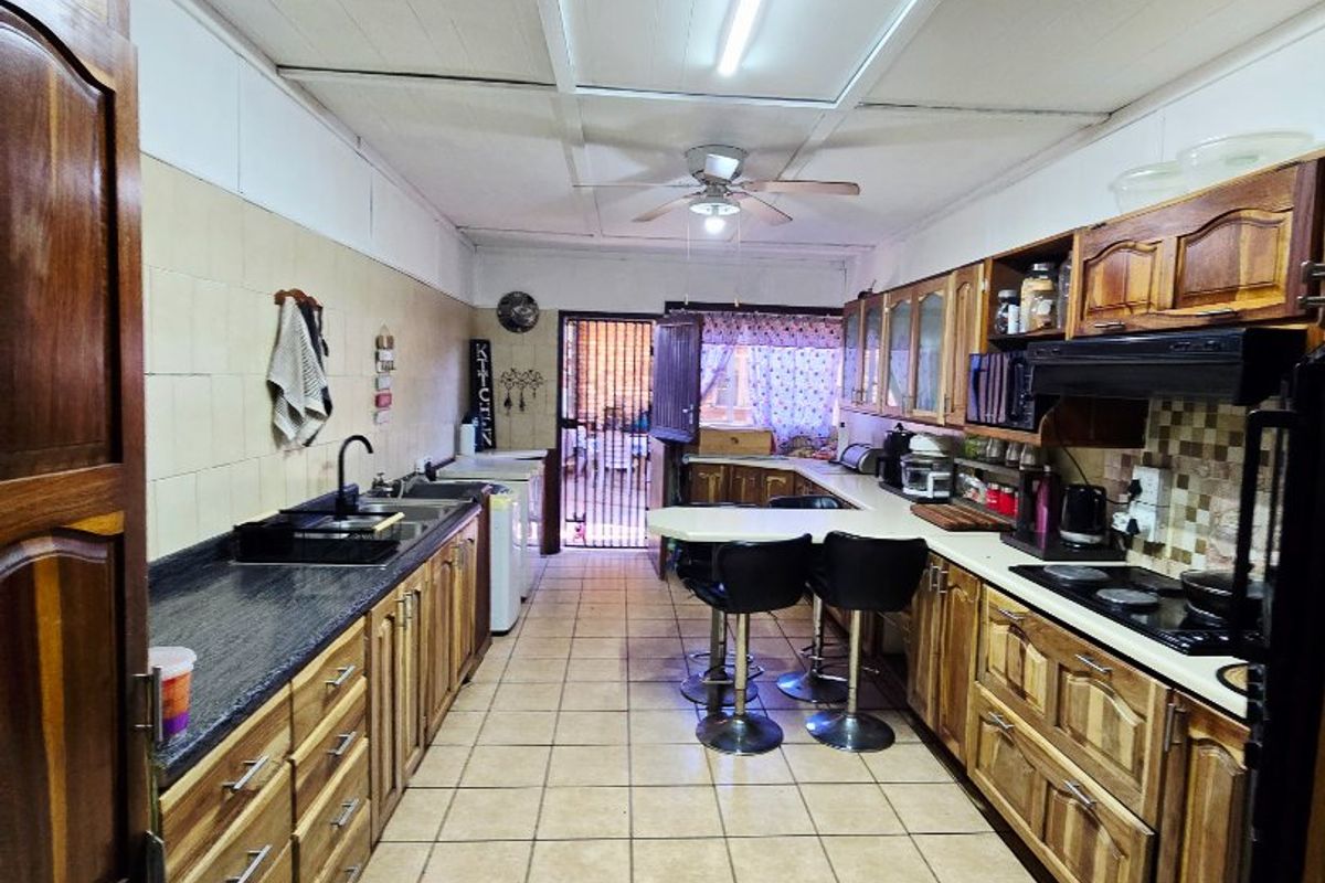 A functional galley-style kitchen featuring extensive wooden cabinetry, granite countertops, built-in cooking appliances, and tiled flooring throughout.