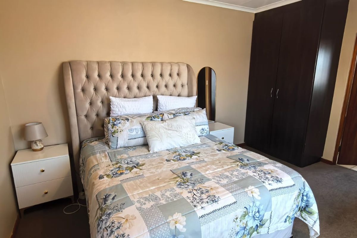 A bedroom featuring neutral wall tones, carpeted flooring, and a dark wood built-in wardrobe with direct access to an adjoining bathroom.