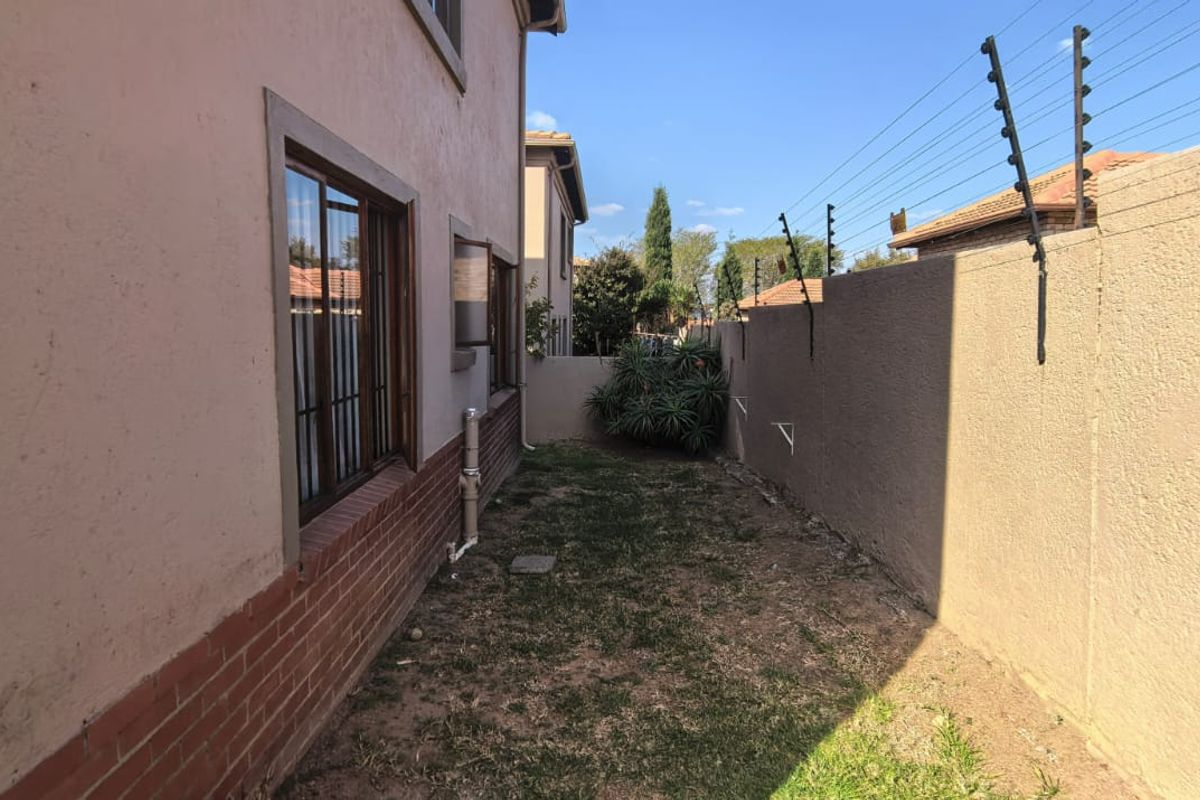 A narrow side garden area featuring a perimeter wall with electric fencing and a brick-based exterior wall finish.