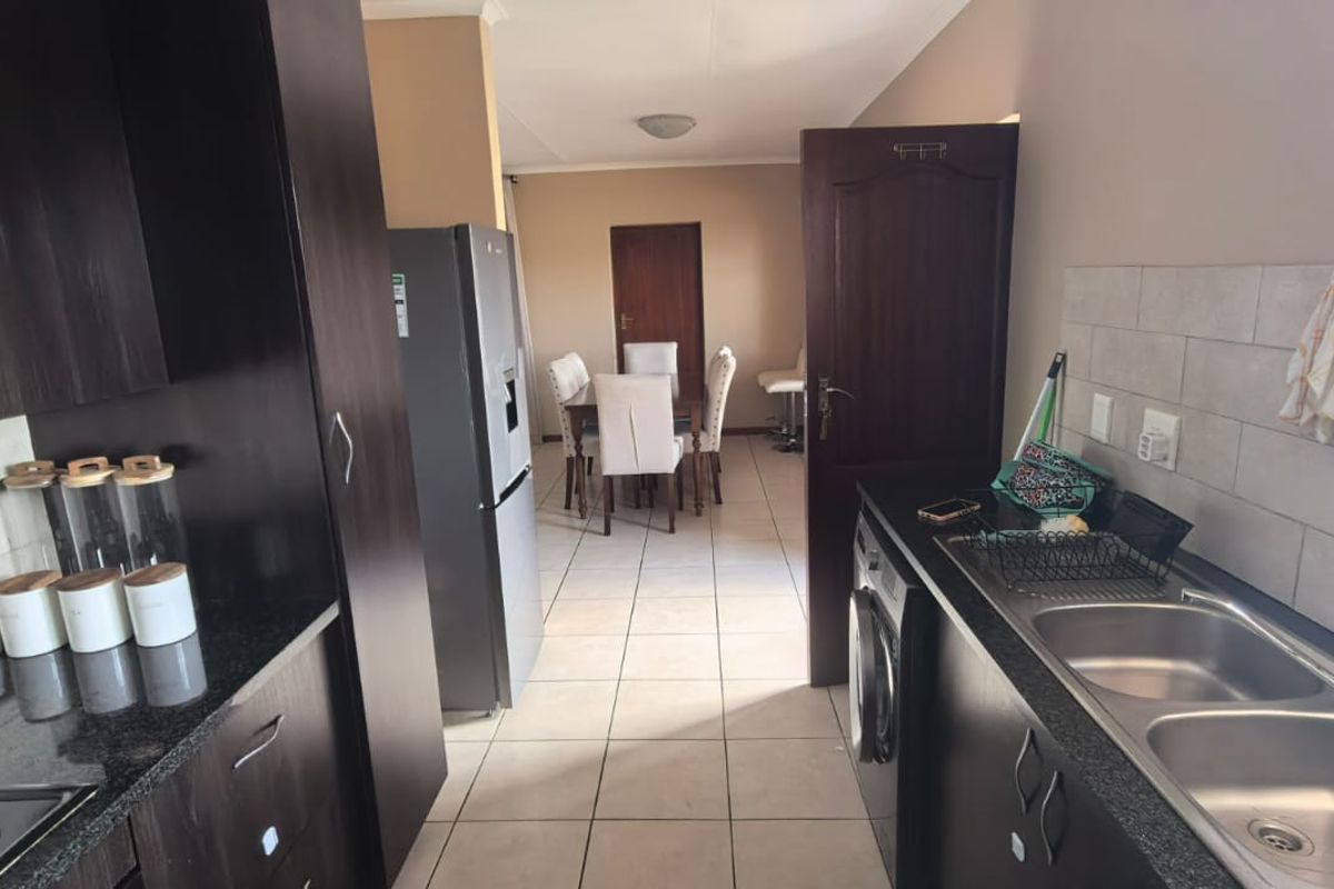 A functional kitchen featuring dark wood cabinetry, granite countertops, a double stainless steel sink, and a built-in hob with an extractor fan.