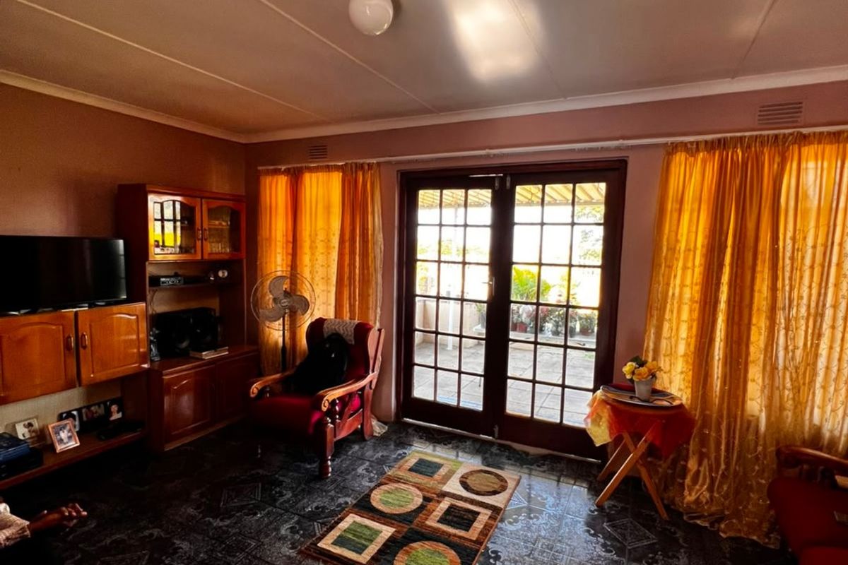 A living room featuring dark patterned floor tiles and glass-paned french doors providing access to an outdoor patio area.