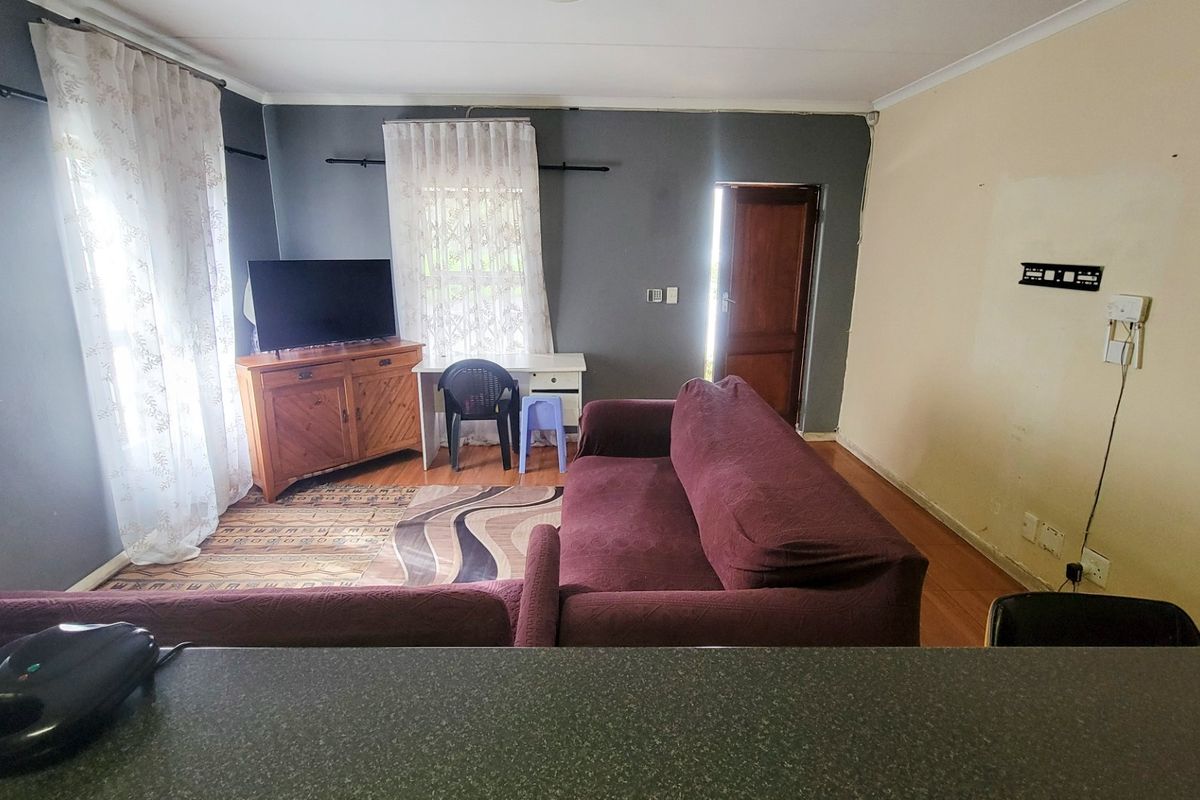 A living room area featuring laminate flooring and direct access to an exterior door, requiring cosmetic updates to the wall finishes.
