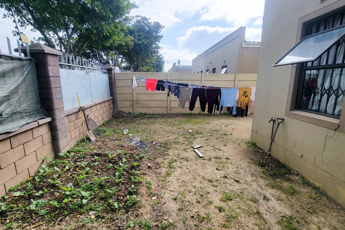 A rear exterior yard area featuring a precast concrete boundary wall with security spikes and a side wall with visible plaster cracking.